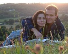 A couple hug and smile while lying in the grass at sunset