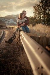 A couple cuddle next to a highway as the sun sets behind them.