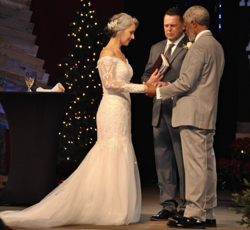 An interracial couple prays with their pastor while being married at a church at Christmas