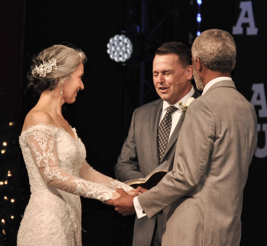 A pastor marries a couple as the bride laughs while holding her husband's hands