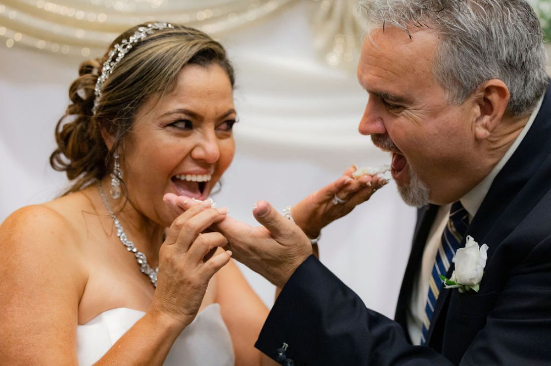 Newlyweds playfully feed each other cake while laughing