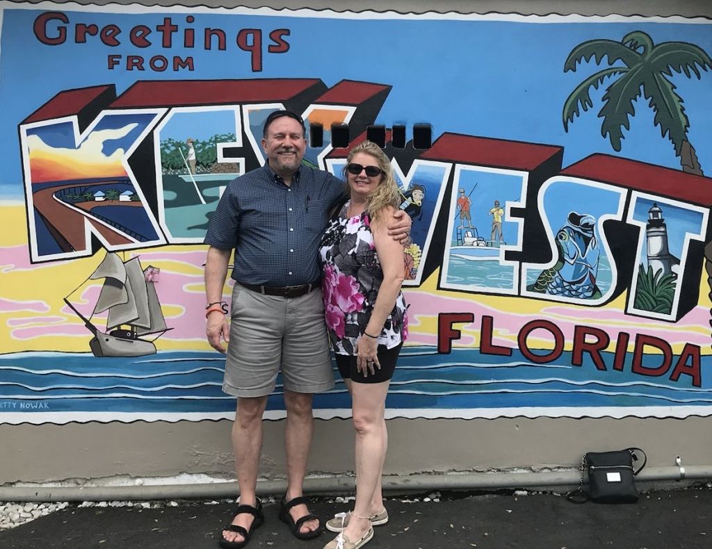 A middle aged Christian couple smile and pose in front of a Key West mural while on honeymoon