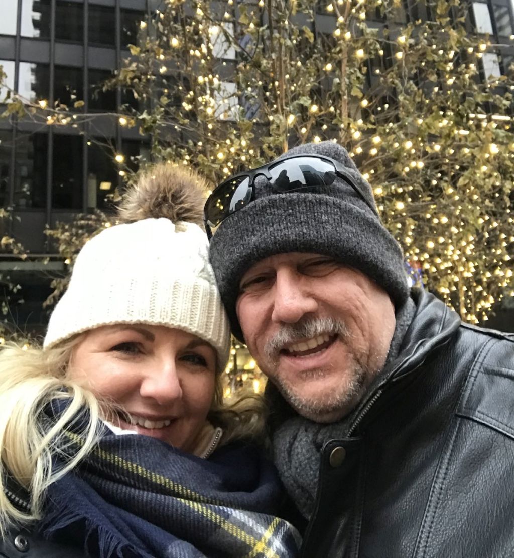 A married Christian couple are bundled up in front of a Christmas tree in Chicago