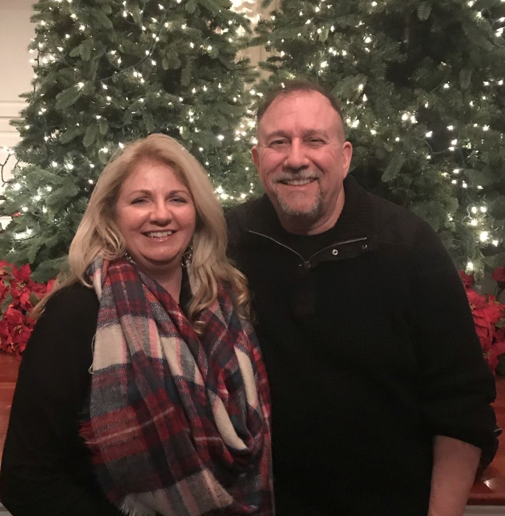 A Christian couple laugh at Christmas time in front of a large display of Christmas trees and poinsettia plants