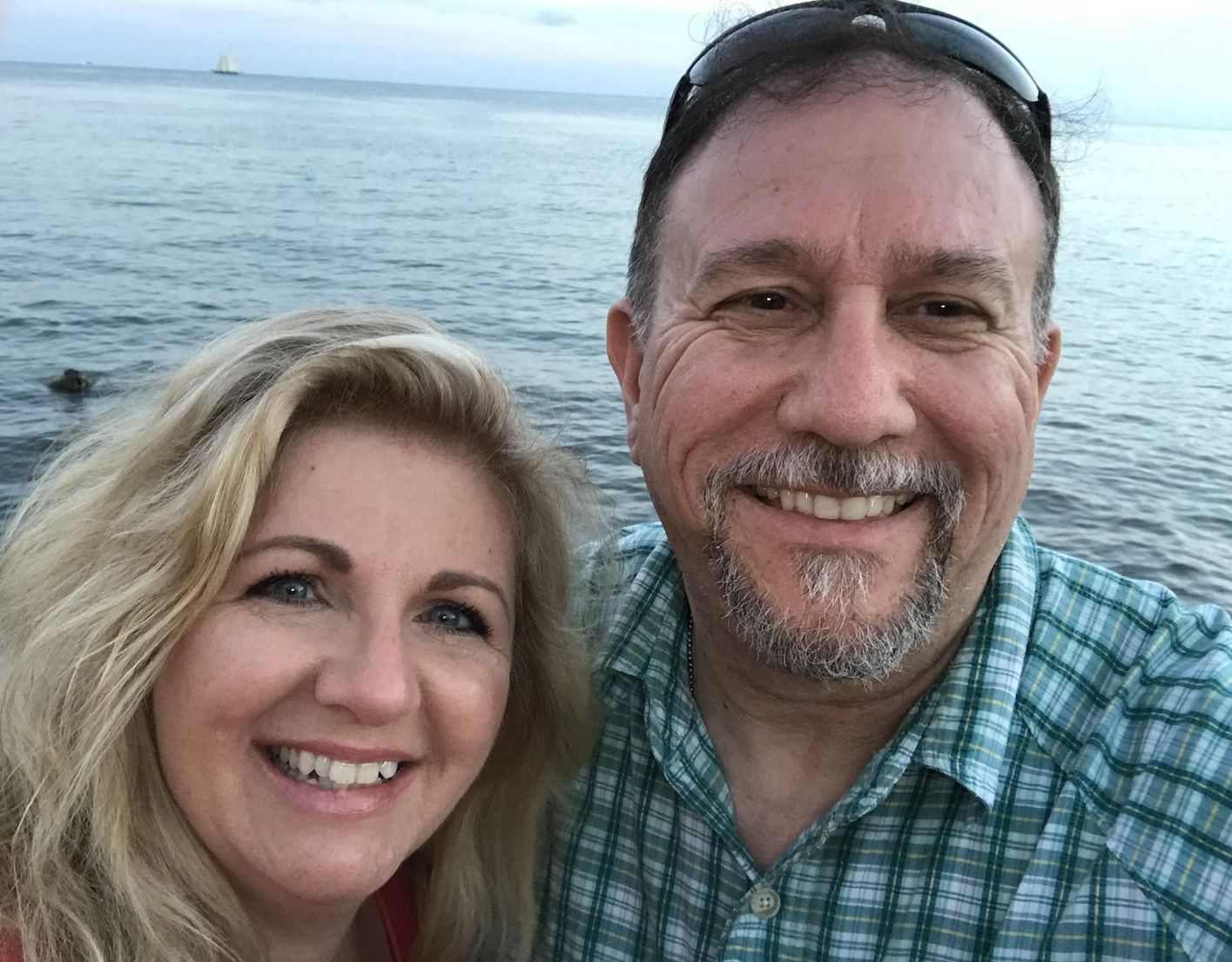 A woman with a beautiful smile poses with her husband in front of the ocean