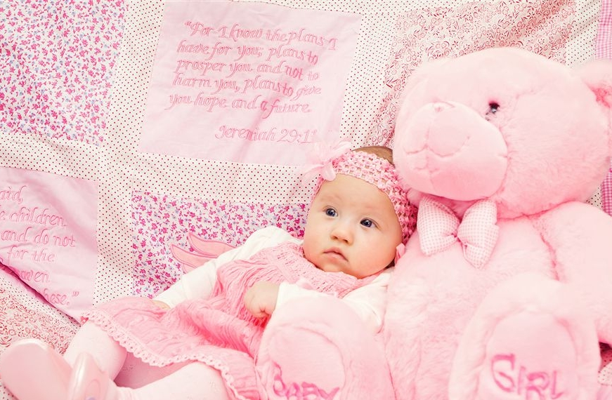 A baby dress in pink leans against a large teddy bear