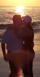 A silhouetted couple kiss at ocean sunset