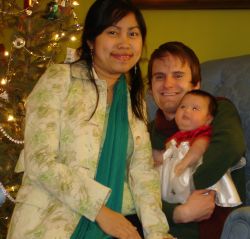Happy Christian couple with their new baby cuddle on the couch in front of Christmas tree