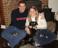 A woman holds her puppy and laughs joyfully as her husband puts his arm around her