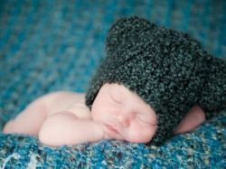 A beautiful baby lies sleeping while wearing a hat