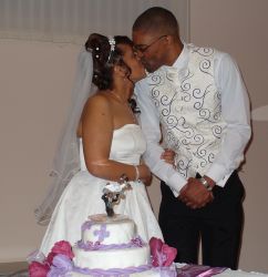 A beautiful British Christian couple kiss lovingly in front of their wedding cake