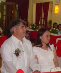 A couple dressed in white sit pensively at a wedding service