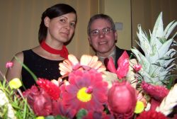 A man laughs while playfully looking over some flowers as he sits next to a beautiful woman