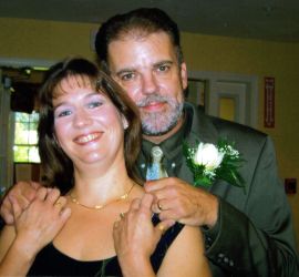 Christian singles no more as a newly married man stands behind his wife, who smiles and holds his hand tenderly