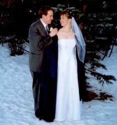 A handsome gentleman wraps a coat around a pretty woman in a white dress in the winter