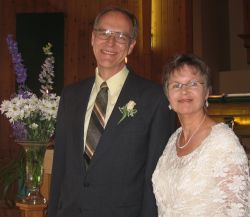 Dave and Patricia smile in front of beautiful flowers on their wedding day