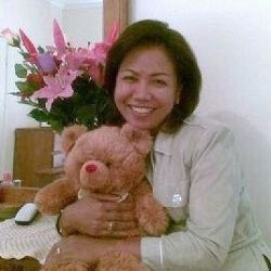 A woman holds a teddy bear and laughs in front of flowers from her Australian boyfriend