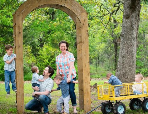 Married couple stand and laugh while holding their children under their wedding arch