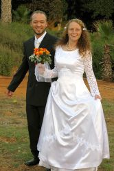 A woman in a beautiful bridal dress holds her bouquet and laughs next to her husband