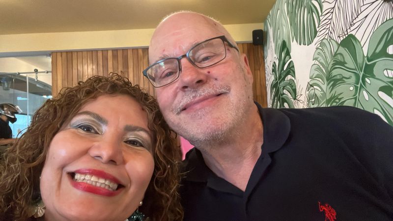 A Latina single Christians smiles with glee as she leans into a White man with glasses