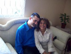 A woman grins wholeheartedly as a man hugs her while seated on a couch