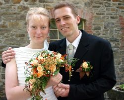 A bride holds up her beautiful flowers as her husband holds her hand