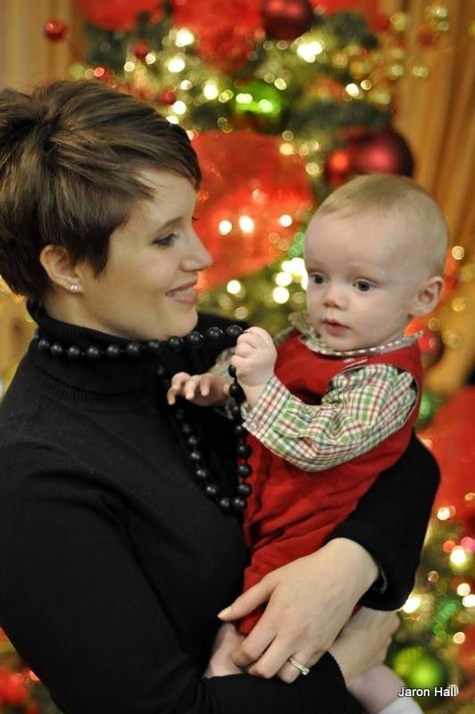 A beautiful Christian mother gazes lovingly a her baby boy in front of a Christmas tree