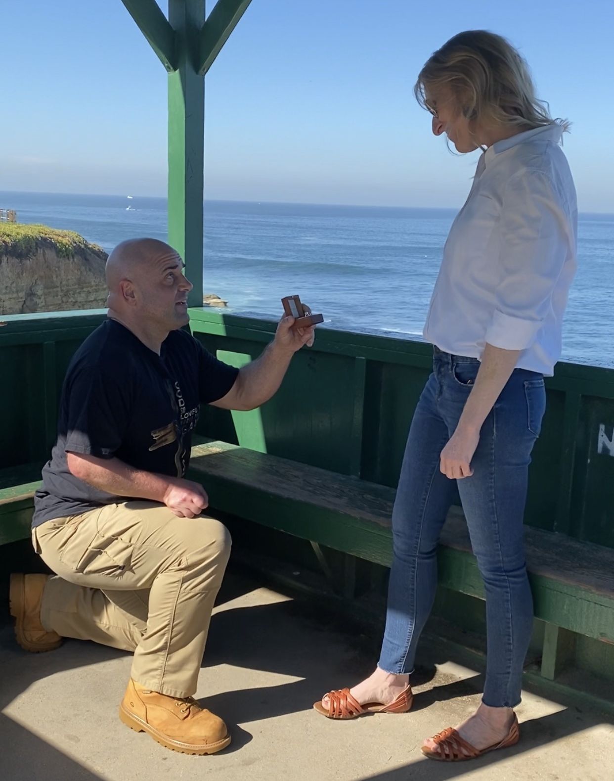 A Christian single man proposes to a blonde woman with the ocean in the background