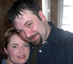 Man with goatee leans his head into a pretty woman, who smiles