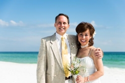 An overjoyed woman holding flowers on a beach is hugged by a well dressed man
