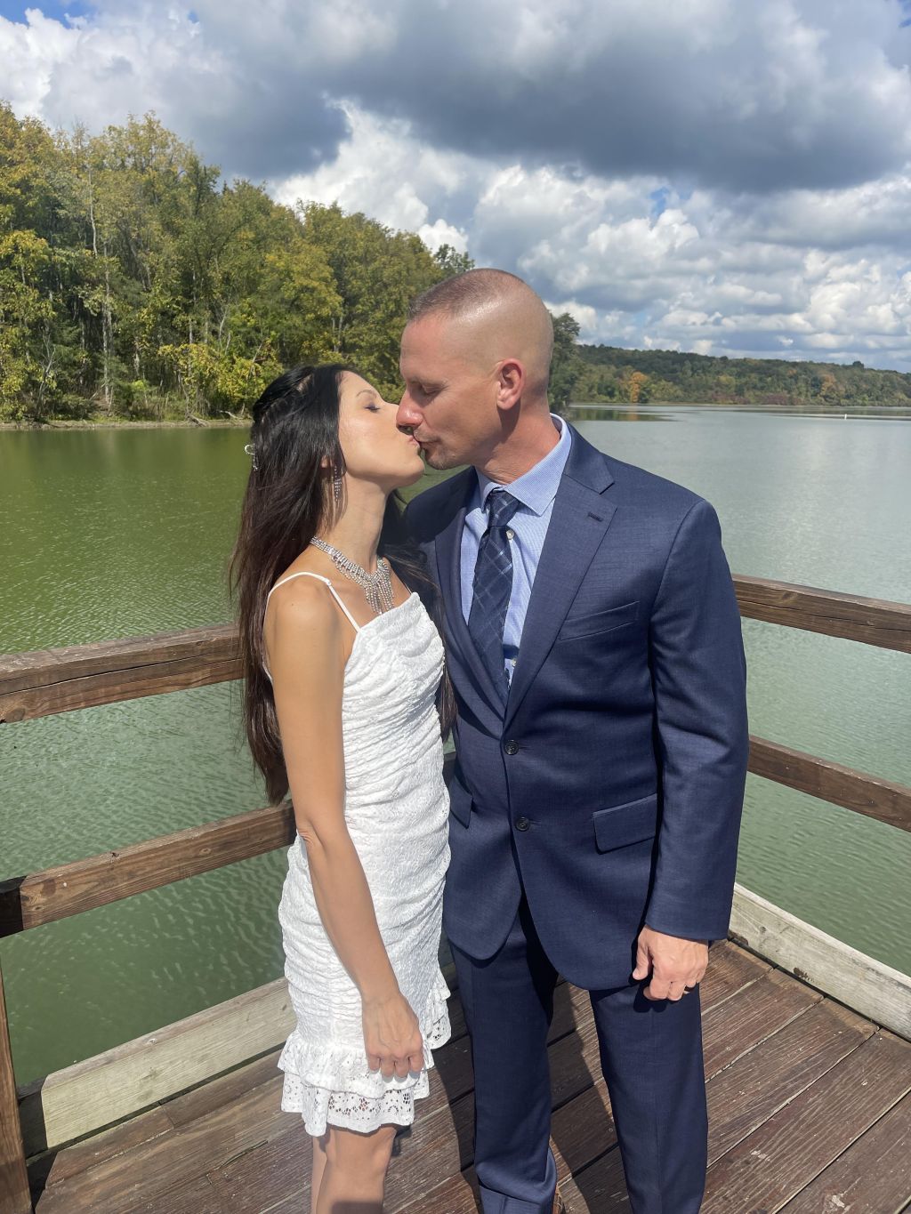 Newly married Christians kiss on a deck by a river on their wedding day
