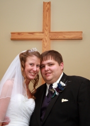 A beautiful young married Christian couple pose under a cross