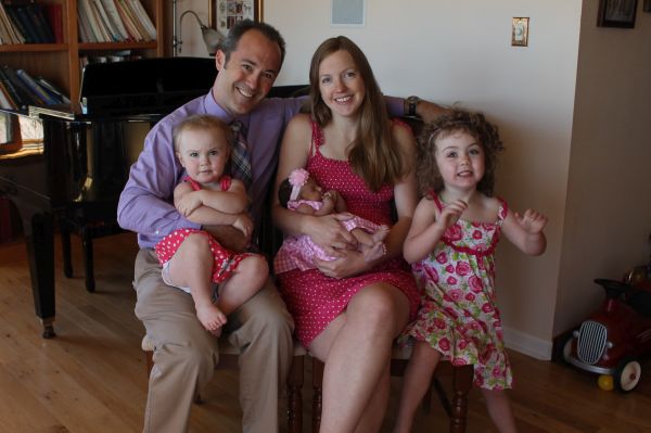 A beautiful mother holds her newborn while her husband laughs with his daughters