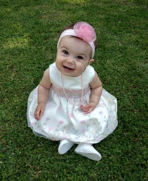 Cute baby girl sitting on grass in white dress and laughing