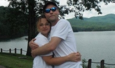 A couple hug outside in front of a beautiful lake