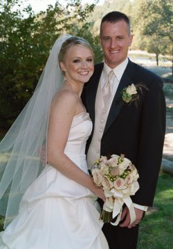 Julie with beautiful wedding dress and flowers stands next to her proud husband
