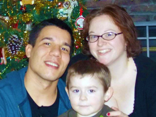 Christmas photo of Christian couple and their son in front of Christian tree