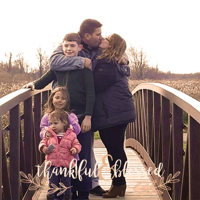 A couple kisses on a bridge while out for a hike with their 3 cute children