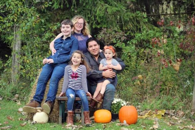 Family seated on a hay bale in front of pumpkins at a fall festival 