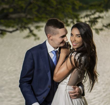 Happy Christian wife smiling at camera while husband holds and looks only at her