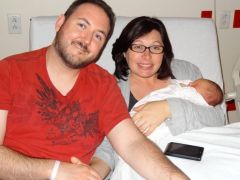 A happy but tired mother holds her newborn after giving birth, while her loving husband holds her hand
