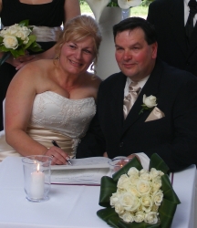 A smiling bride signs her wedding register with her husband
