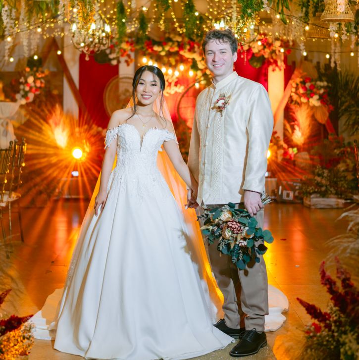 Newly married Christians pose together in a beautiful setting of flowers, streamers, chandeliers, and golden light bathing the scene