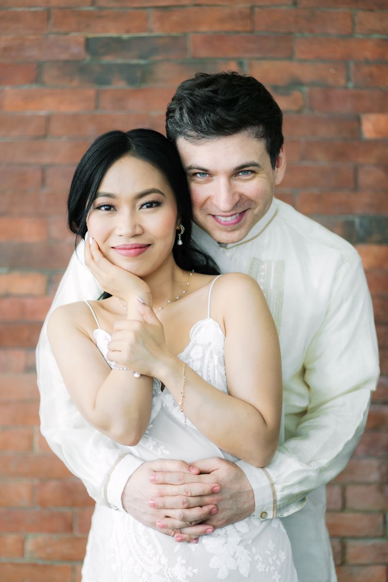 A White Christian man wraps his arms around a beautiful Asian woman who smiles confidently