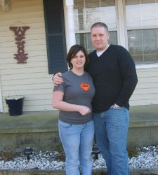 Bible college graduate stands with his arm around his wife in front of their house