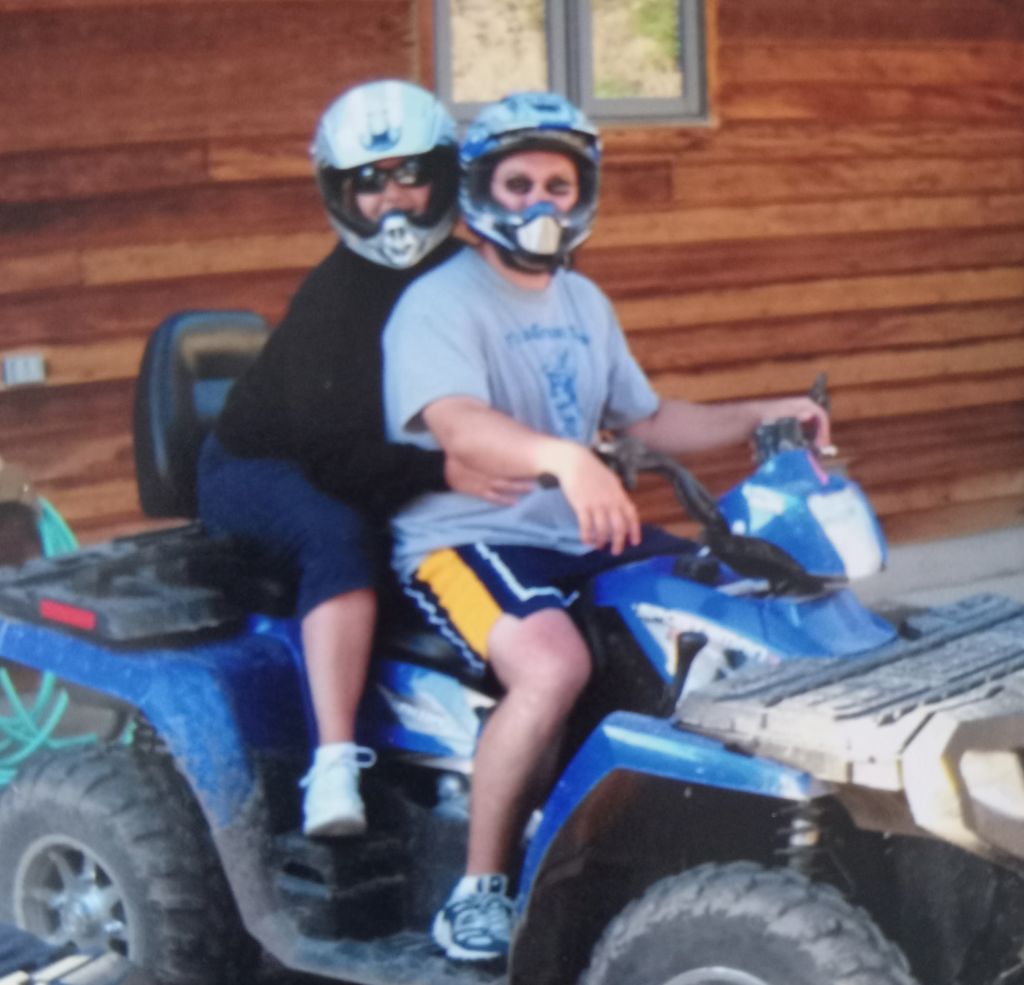 A Christian couple in helmets sit atop an ATV in front of a cabin