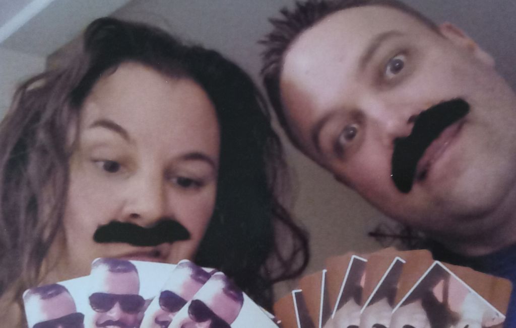 A couple wears fake moustaches and acts silly in front of camera