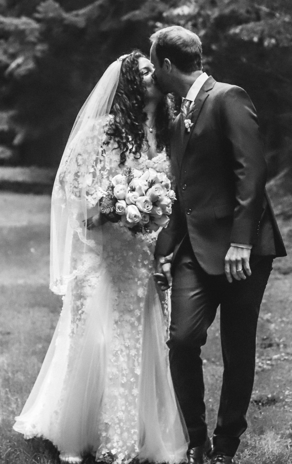 A black and white photo of newly married Christians kissing. The bride is in her wedding dress and holding flowers.