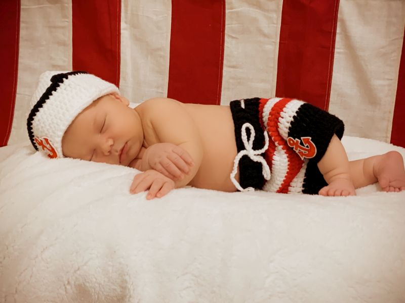 Baby lies sleeping on a white sheet with American flag behind