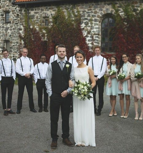 Huge wedding party poses behind bride and groom in front of old stone arches